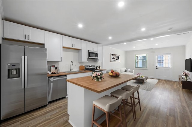 kitchen featuring a kitchen breakfast bar, butcher block countertops, a kitchen island, white cabinetry, and stainless steel appliances