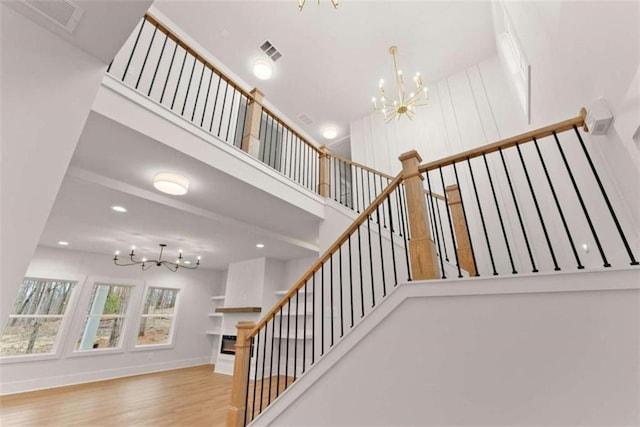 staircase with baseboards, visible vents, a towering ceiling, wood finished floors, and a notable chandelier