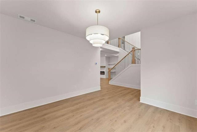 empty room with light wood-style floors, visible vents, stairway, and baseboards