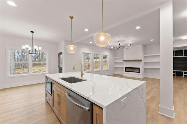 kitchen with pendant lighting, appliances with stainless steel finishes, a glass covered fireplace, a sink, and light wood-type flooring