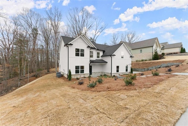 view of front of house with a shingled roof, dirt driveway, central AC unit, stone siding, and board and batten siding