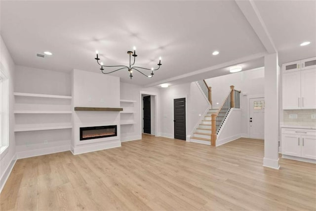 unfurnished living room with a notable chandelier, baseboards, light wood-style floors, stairway, and a glass covered fireplace