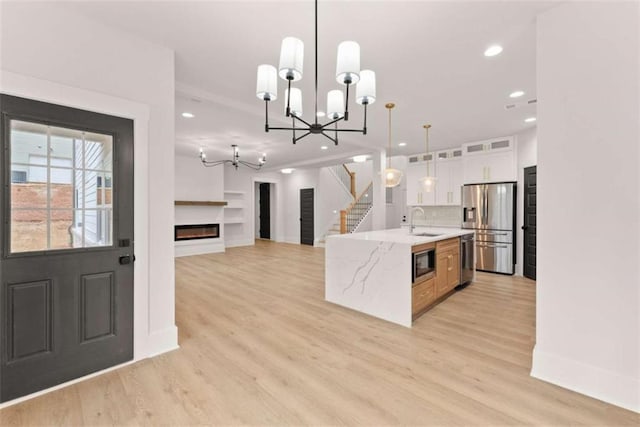 kitchen with light wood-style flooring, appliances with stainless steel finishes, a glass covered fireplace, white cabinets, and a sink