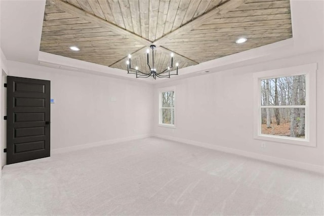 carpeted empty room with a tray ceiling, wood ceiling, a notable chandelier, and baseboards