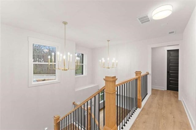 corridor with a chandelier, visible vents, an upstairs landing, and light wood-style floors