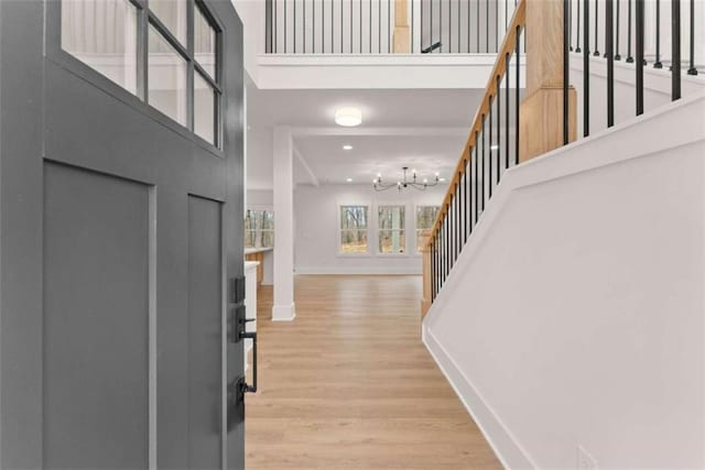 foyer with baseboards, light wood-style flooring, stairway, a high ceiling, and a notable chandelier