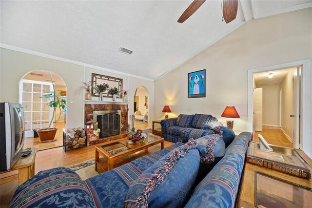 living room with ceiling fan, a high end fireplace, high vaulted ceiling, hardwood / wood-style flooring, and ornamental molding