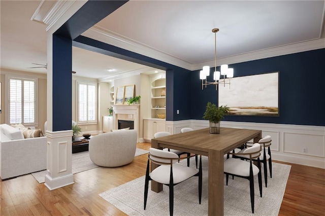 dining room featuring built in shelves, light hardwood / wood-style flooring, ceiling fan with notable chandelier, and ornamental molding