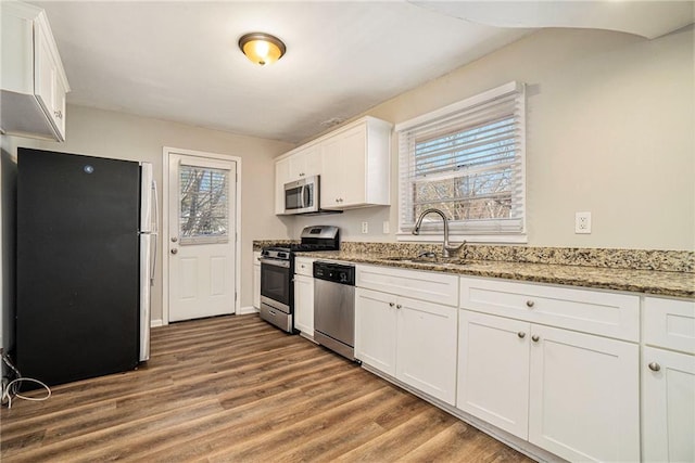 kitchen with light stone countertops, stainless steel appliances, a healthy amount of sunlight, sink, and white cabinetry