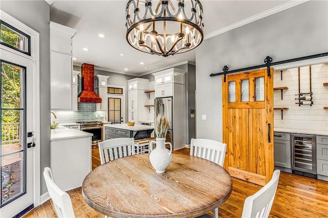 dining space featuring beverage cooler, ornamental molding, light wood-style flooring, and a barn door