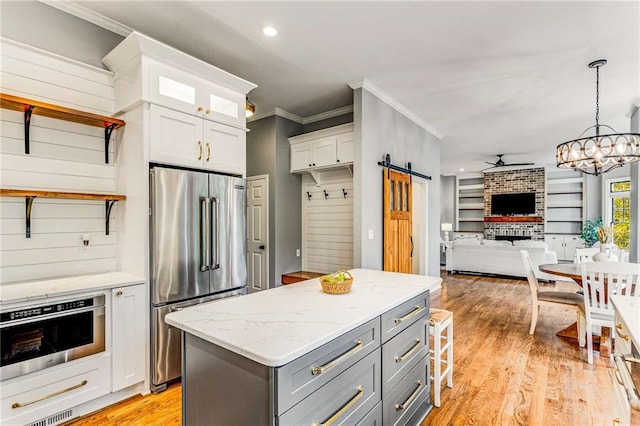 kitchen with a barn door, gray cabinetry, stainless steel appliances, light wood-style floors, and white cabinets