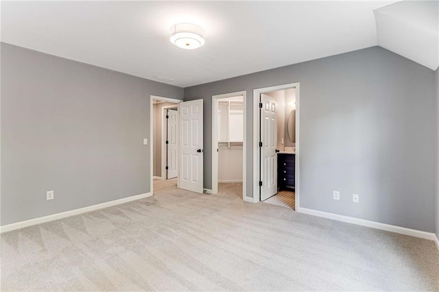 unfurnished bedroom featuring baseboards, vaulted ceiling, a walk in closet, carpet floors, and a closet