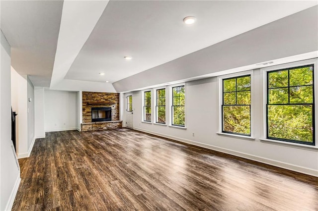 unfurnished living room with dark wood-style floors, a stone fireplace, lofted ceiling, and baseboards