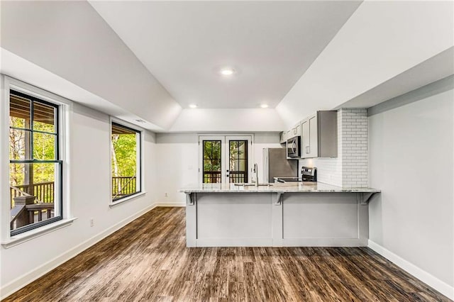 kitchen with baseboards, decorative backsplash, appliances with stainless steel finishes, dark wood-style flooring, and a peninsula