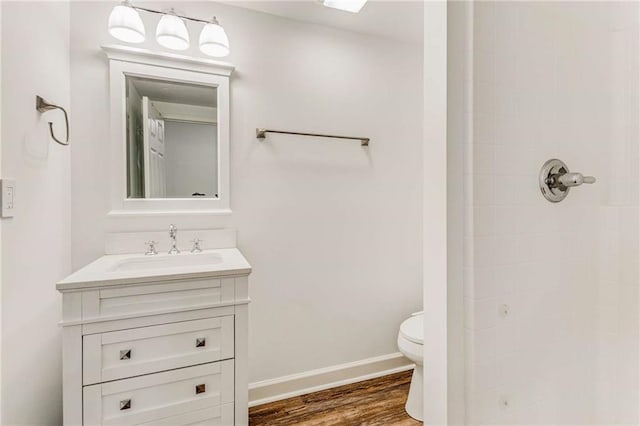 full bathroom featuring baseboards, toilet, wood finished floors, a tile shower, and vanity