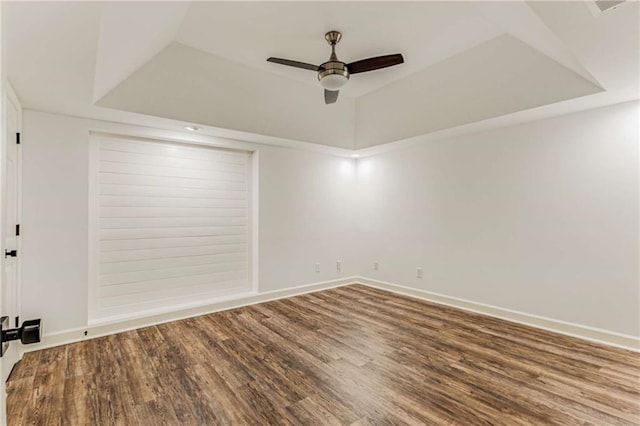 unfurnished room with a tray ceiling, wood finished floors, a ceiling fan, and baseboards