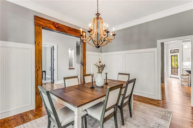 dining area with light wood-style floors, a wainscoted wall, crown molding, and a notable chandelier