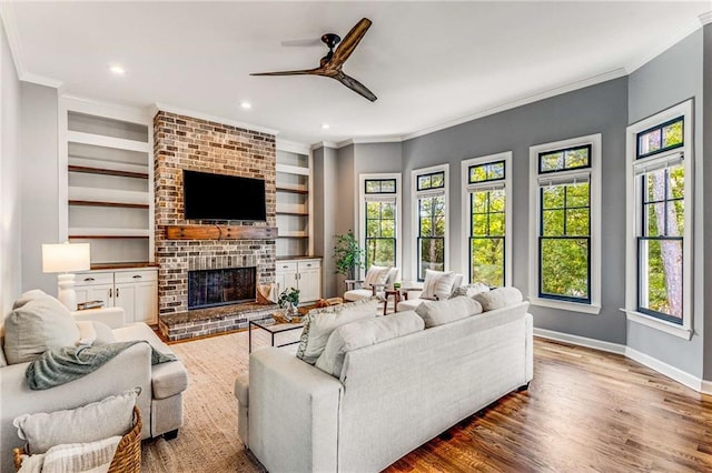 living room featuring built in features, a fireplace, crown molding, wood finished floors, and baseboards