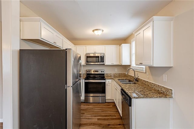 kitchen featuring a sink, white cabinetry, appliances with stainless steel finishes, dark stone counters, and dark wood finished floors