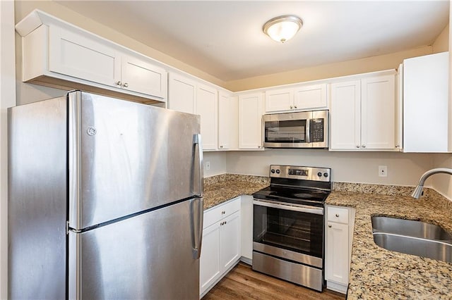 kitchen with light stone counters, appliances with stainless steel finishes, a sink, and white cabinetry