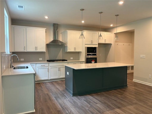 kitchen featuring visible vents, light countertops, wall chimney exhaust hood, a sink, and dark wood finished floors
