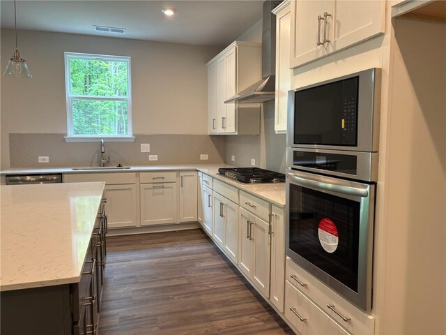 kitchen with visible vents, wall chimney exhaust hood, white cabinetry, a sink, and stainless steel appliances