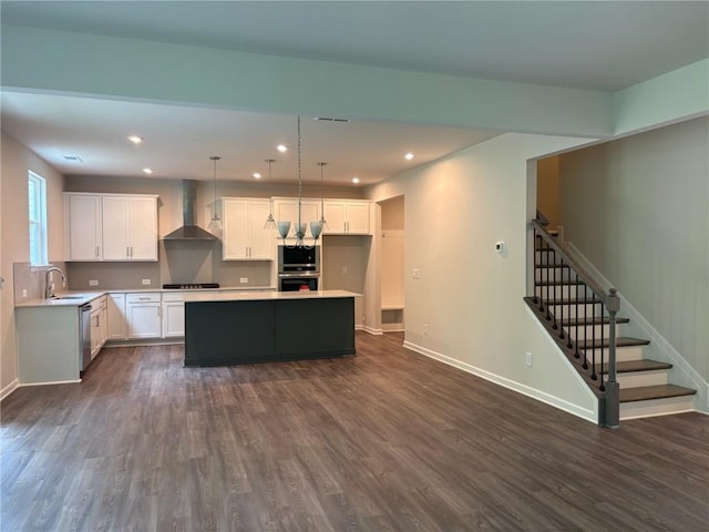 kitchen featuring wall chimney range hood, a center island, a sink, and dark wood-type flooring