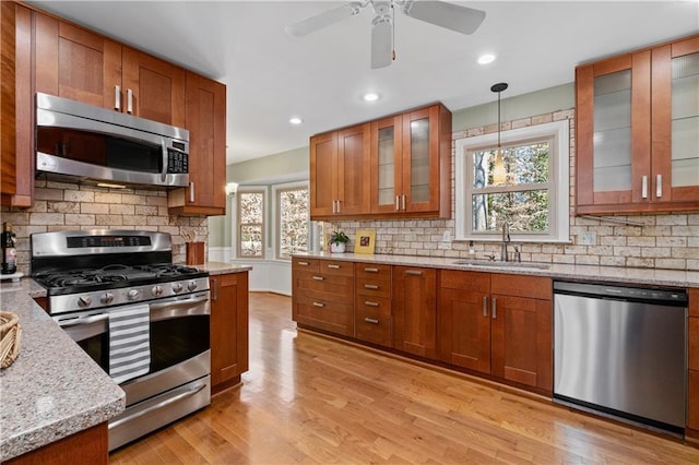 kitchen featuring appliances with stainless steel finishes, decorative light fixtures, sink, light wood-type flooring, and light stone counters