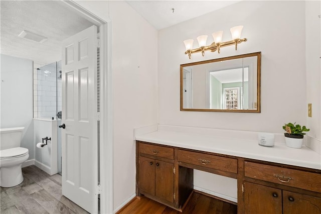 bathroom with hardwood / wood-style flooring, toilet, vanity, and a tile shower