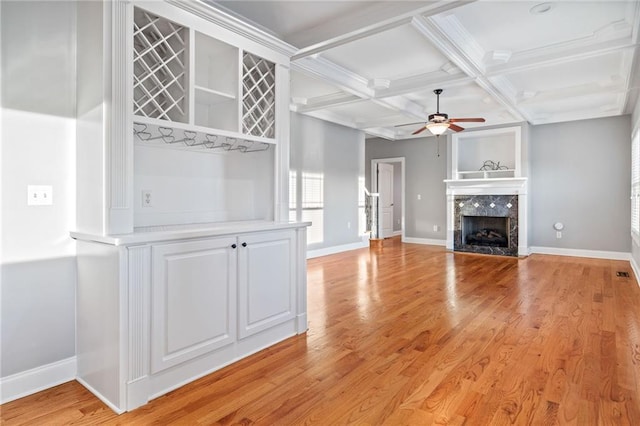 unfurnished living room featuring beamed ceiling, coffered ceiling, ceiling fan, a high end fireplace, and light hardwood / wood-style flooring