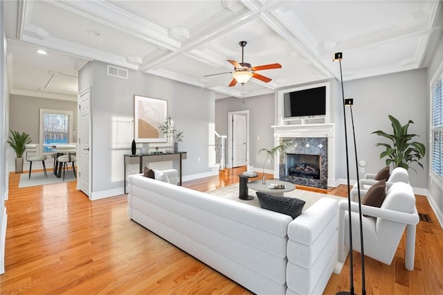 living room with ornamental molding, coffered ceiling, a premium fireplace, beam ceiling, and light hardwood / wood-style flooring