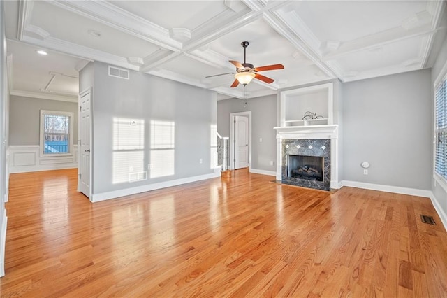 unfurnished living room featuring light hardwood / wood-style flooring, ceiling fan, coffered ceiling, ornamental molding, and a tiled fireplace