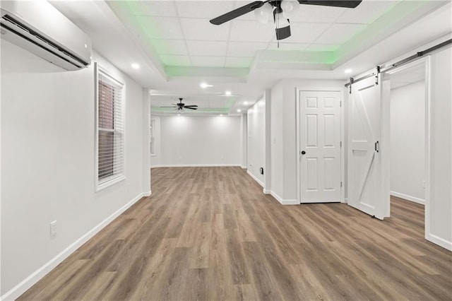 hall featuring a drop ceiling, a raised ceiling, a barn door, an AC wall unit, and wood-type flooring