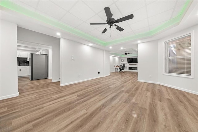 unfurnished living room with light hardwood / wood-style floors, a drop ceiling, and ceiling fan