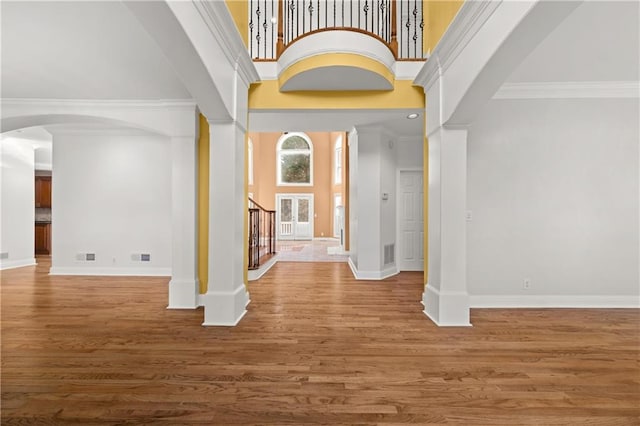 entryway featuring hardwood / wood-style flooring, ornamental molding, a high ceiling, and ornate columns