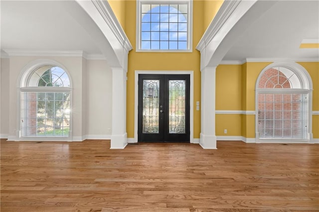 entrance foyer featuring french doors, light wood-type flooring, ornamental molding, and a high ceiling