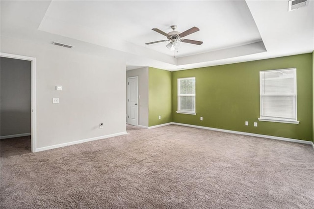 carpeted spare room with a tray ceiling, baseboards, visible vents, and a ceiling fan
