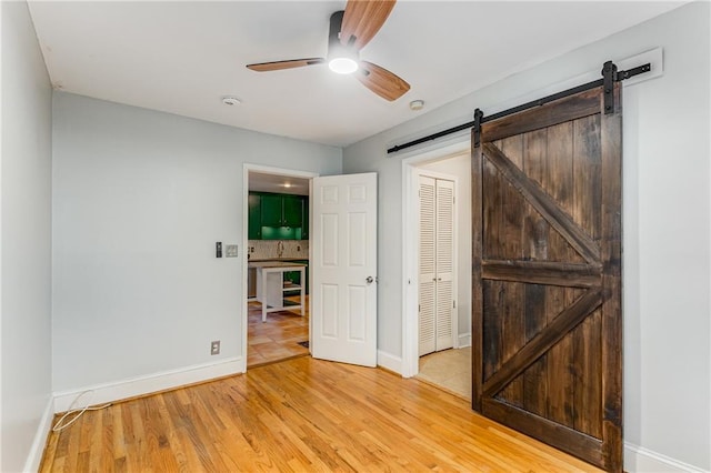 unfurnished bedroom featuring a barn door, baseboards, a ceiling fan, light wood-type flooring, and a closet