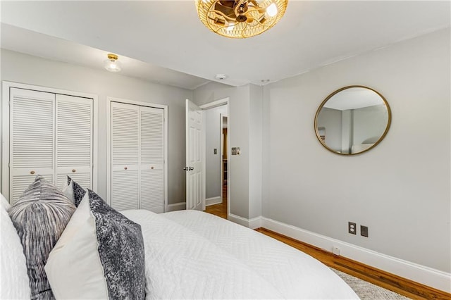 bedroom featuring multiple closets, baseboards, and wood finished floors