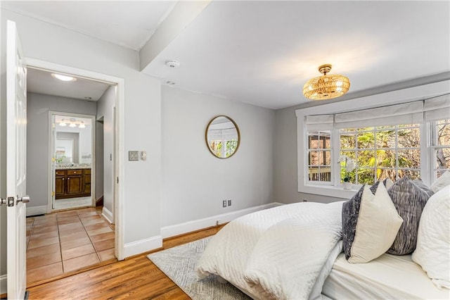 bedroom with light wood-style floors, baseboards, and connected bathroom