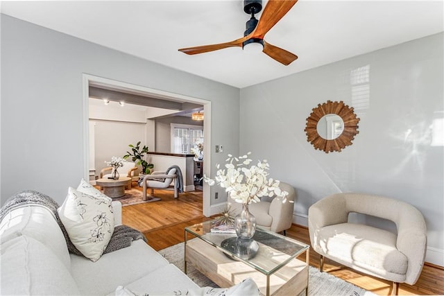 living room with ceiling fan, baseboards, and wood finished floors