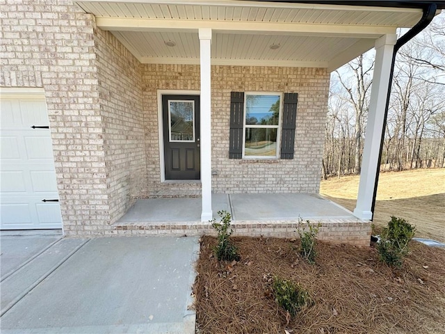 view of exterior entry with a porch, brick siding, and a garage