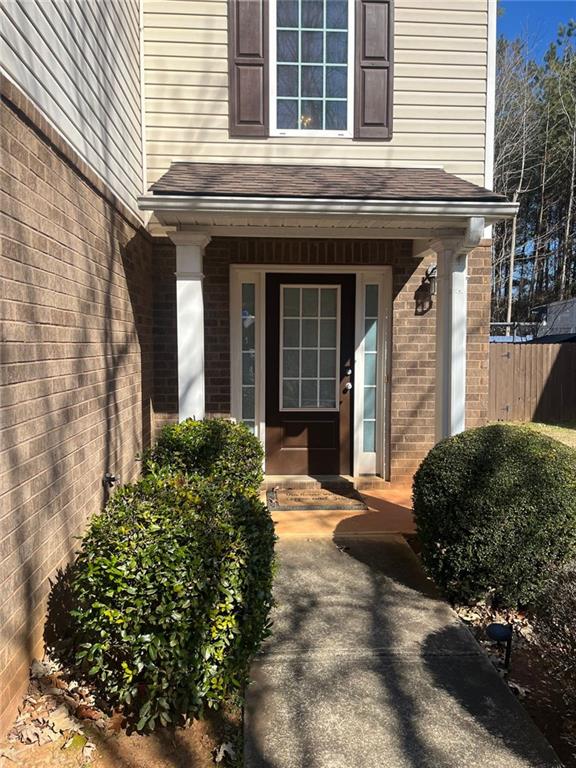 property entrance featuring covered porch, a shingled roof, fence, and brick siding