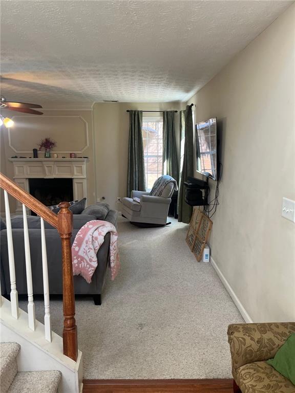 living room featuring a ceiling fan, carpet flooring, a fireplace, and stairs