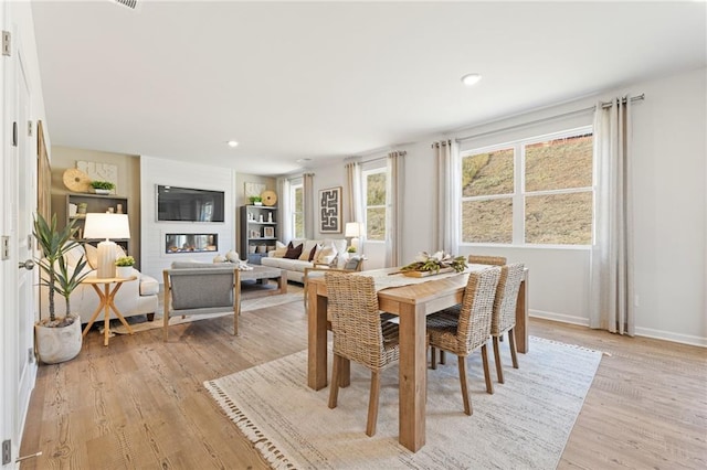 dining space with a glass covered fireplace, baseboards, light wood-style flooring, and recessed lighting