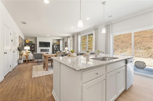 kitchen featuring visible vents, a center island with sink, a sink, stainless steel dishwasher, and light wood finished floors