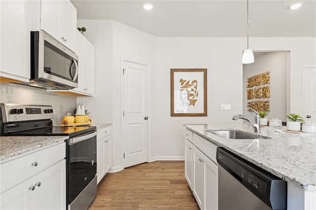 kitchen featuring light wood finished floors, backsplash, appliances with stainless steel finishes, white cabinetry, and a sink