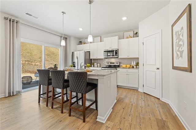 kitchen with visible vents, a breakfast bar, an island with sink, decorative backsplash, and appliances with stainless steel finishes