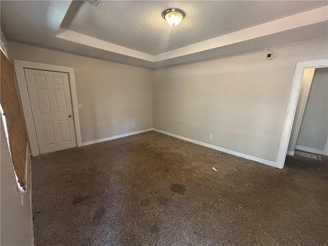 unfurnished room with a textured ceiling, a raised ceiling, baseboards, and carpet floors