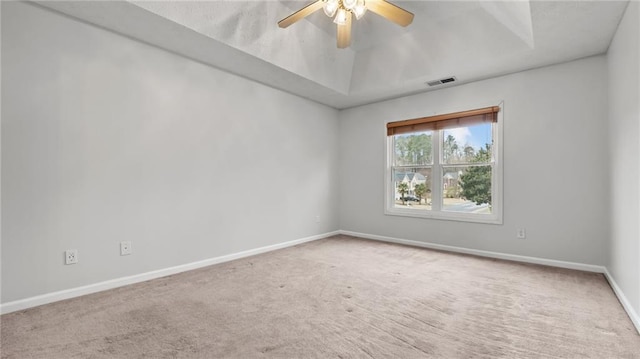 carpeted empty room with a ceiling fan, a raised ceiling, visible vents, and baseboards